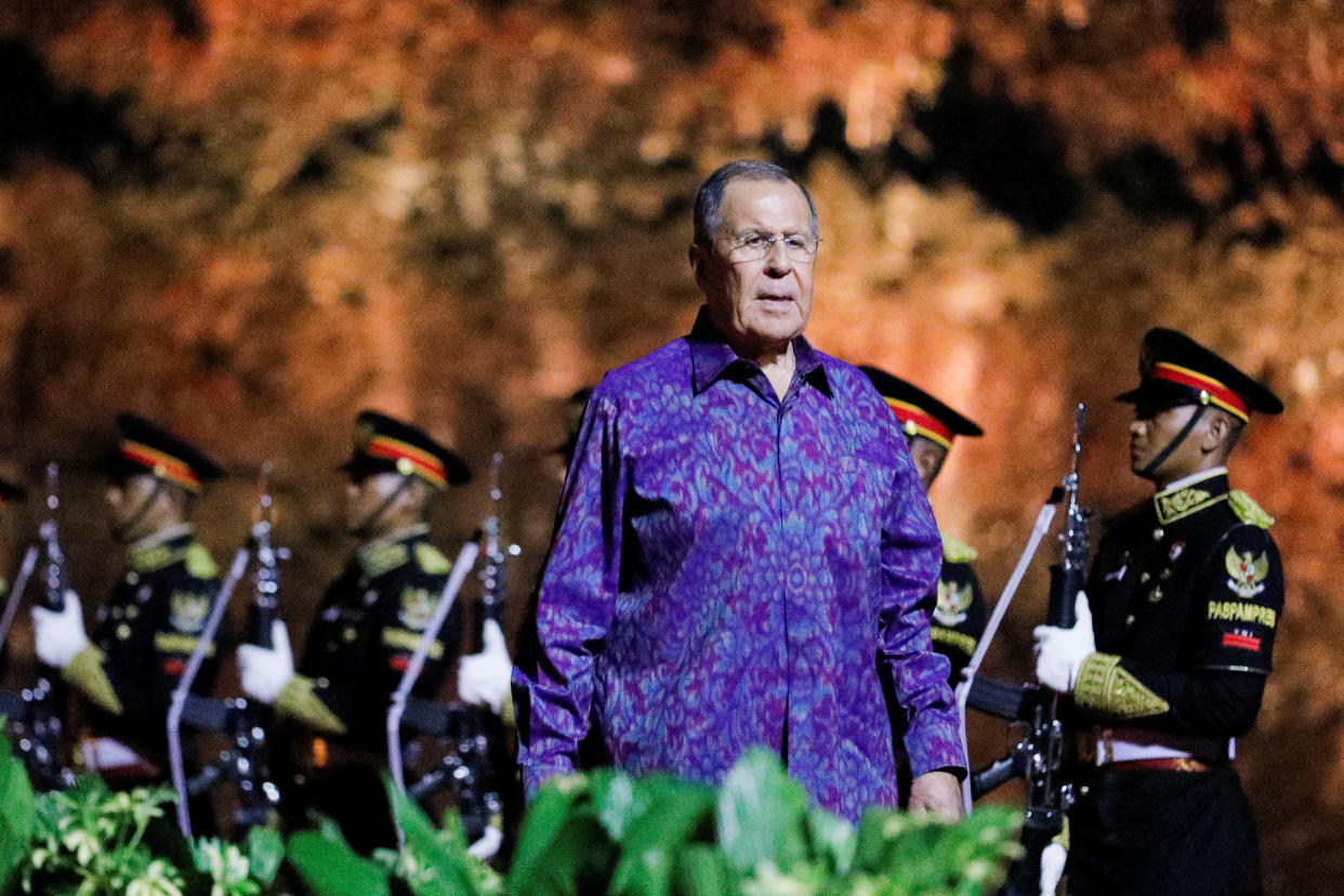 Sergey Lavrov wears what appears to be a traditional Indonesian shirt as he walks by a row of armed guards.