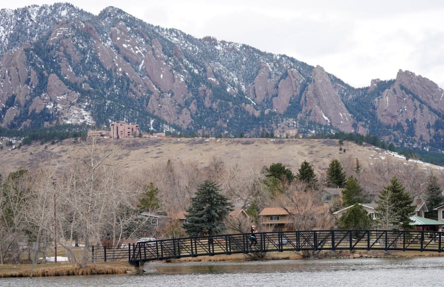 A lone jogger moves across a bridge over the lake in Harlow Platts Community Park with the Flatirons in the background
