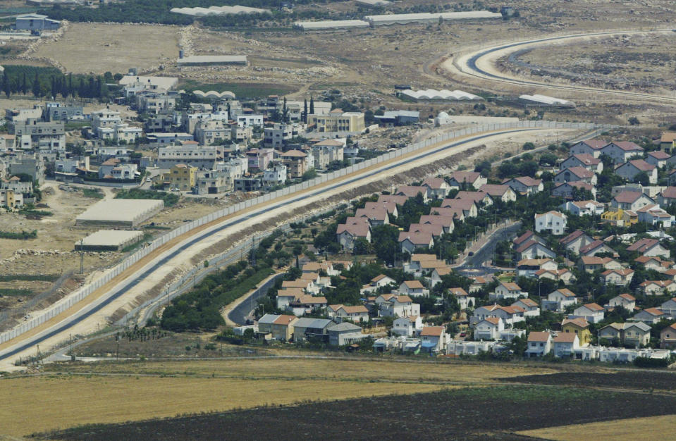 FILE - This aerial view shows a Palestinian village, left, and a Jewish settlement, right, separated by a wall, part of the separation barrier, in the West Bank, July 29, 2003. Israel on Monday, Jan. 31, 2022, called on Amnesty International not to publish an upcoming report accusing it of apartheid, saying the conclusions of the London-based international human rights group are “false, biased and antisemitic.” (AP Photo/Lefteris Pitarakis, File)