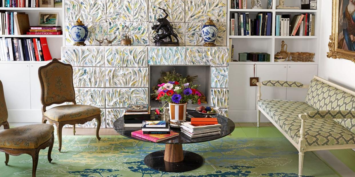 library with large tiled wall with inset for a planter and built in bookshelves on either side and some chairs and a settee in a chain link pattern upholstery and a round low pedestal table at center heaped with books on a green rung