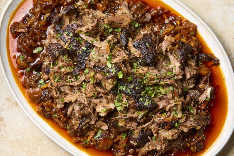 overhead shot of braised moroccan lamb on a large white platter, topped with herbs