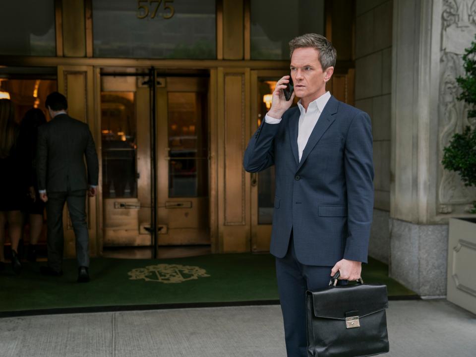 Neil Patrick Harris standing on the phone with a blue suit and briefcase