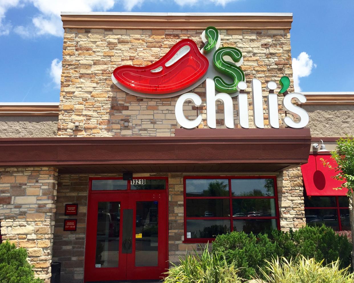 Closeup of front exterior of a Chili's Grill & Bar in Jacksonville, Florida, red doors, surrounded by shrubbery against a bright blue sky with white clouds