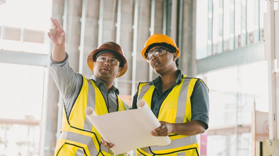 Two multi-ethnic construction workers discussing floor plans.