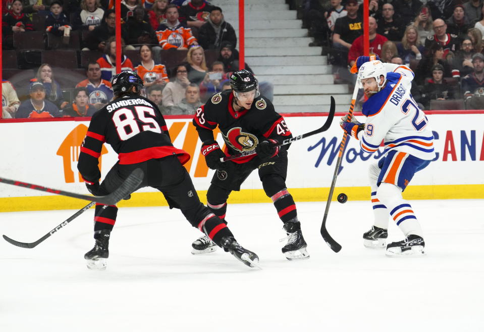 Ottawa Senators left wing Parker Kelly (45) and Edmonton Oilers center Leon Draisaitl (29) vie for the puck as Senators' Jake Sanderson (85) looks on during the first period of an NHL hockey game in Ottawa on Saturday, Feb. 11, 2023. (Sean Kilpatrick/The Canadian Press via AP)
