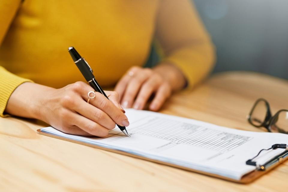 Closeup shot of an unrecognizable woman filling in paperwork on a clipboard at a table