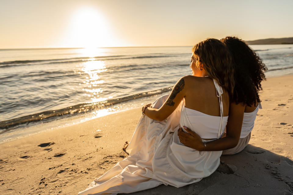 Two women embrace sat on a beach together