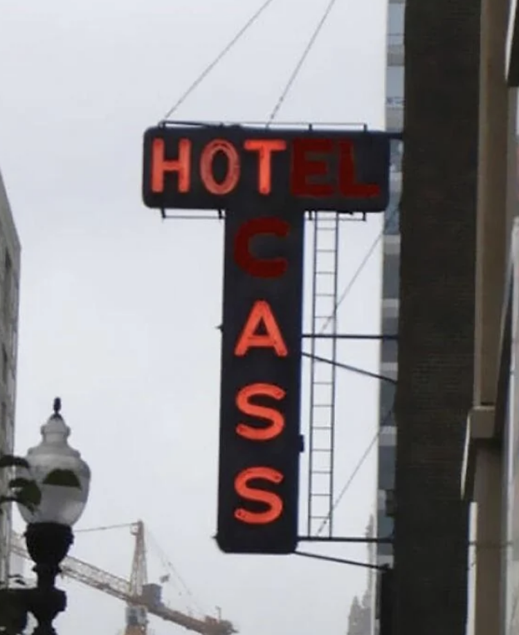 Hotel Cass neon sign mounted vertically on the side of a building in an urban area. A street lamp and construction crane are visible in the background