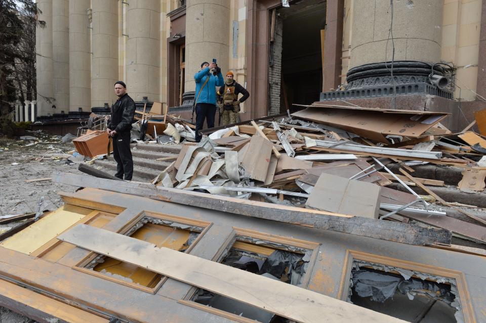 Armed men stand outside the damaged local city hall of Kharkiv on March 1, 2022, destroyed as a result of Russian troop shelling. - The central square of Ukraine's second city, Kharkiv, was shelled by advancing Russian forces who hit the building of the local administration, regional governor Oleg Sinegubov said. Kharkiv, a largely Russian-speaking city near the Russian border, has a population of around 1.4 million. (Photo by Sergey BOBOK / AFP) (Photo by SERGEY BOBOK/AFP via Getty Images)