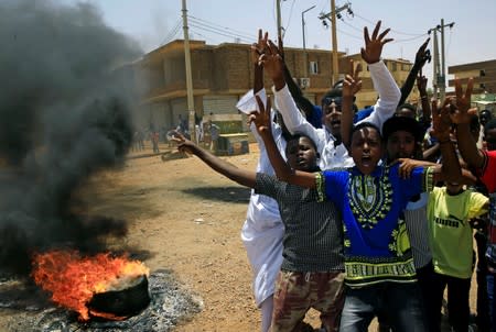 Sudanese protesters gesture and chant slogans at a barricade along a street, demanding that the country's Transitional Military Council hand over power to civilians, in Khartoum