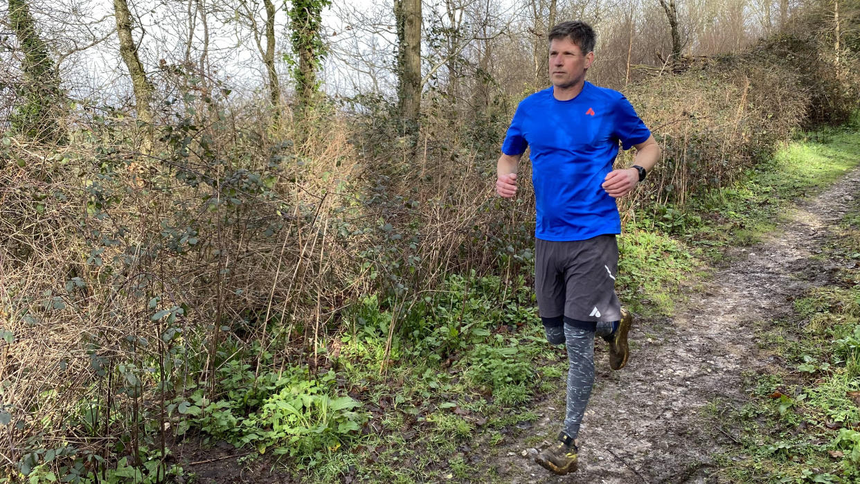  A man wearing Saxx Roast Master Mid-Weight Tights runs along a woody trail. 