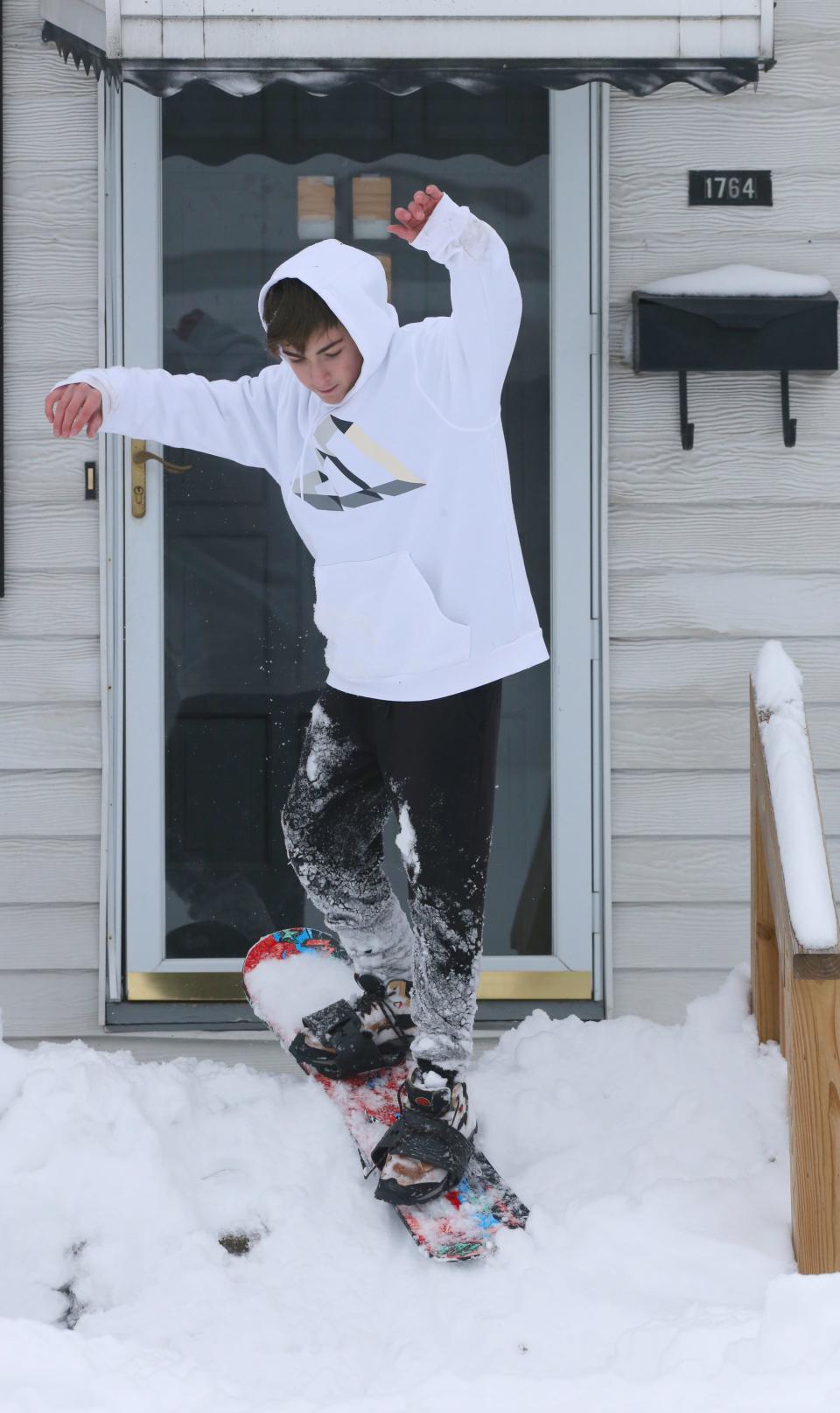 AJ Stair snowboards down a makeshift ramp on his front porch Monday in Cuyahoga Falls.