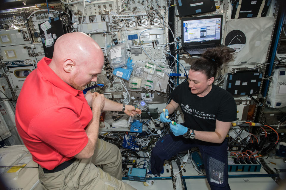 an astronaut on the international space station holds out their arm to another astronaut who is holding medical equipment