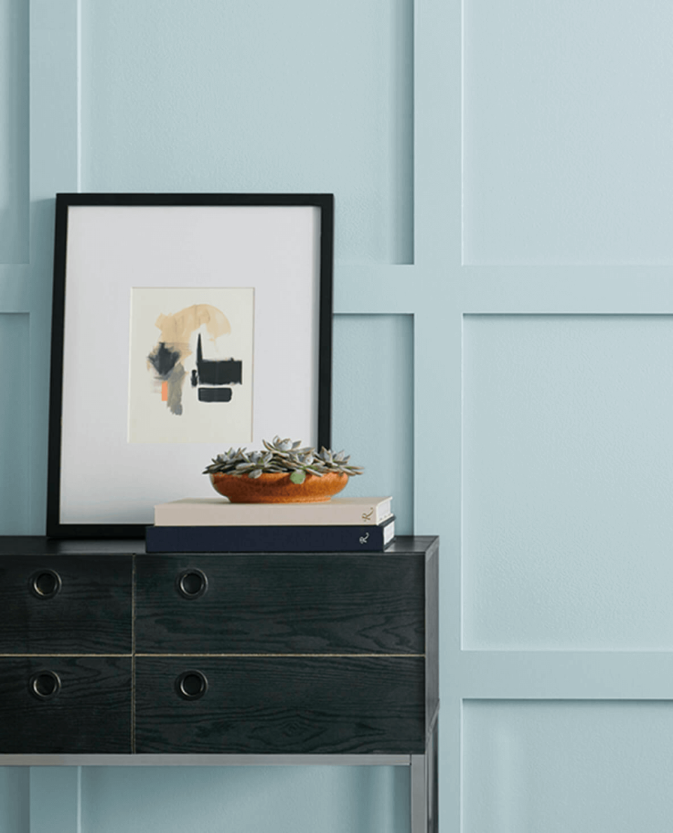 Entry table with artwork and small plant against a wall painted in Sleepy Blue by Sherwin-Williams.