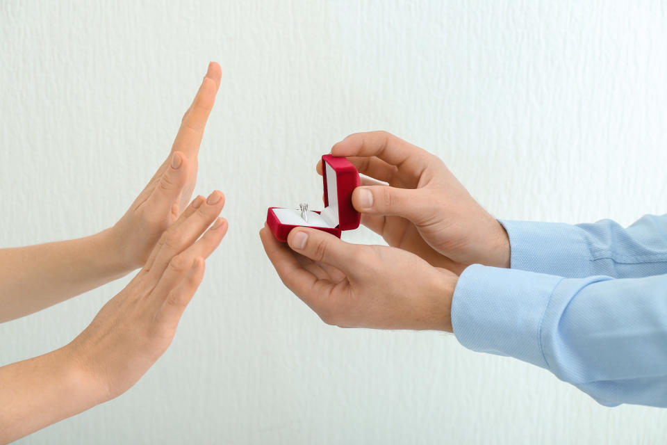 Hands held up "no" in response to hands holding an engagement ring