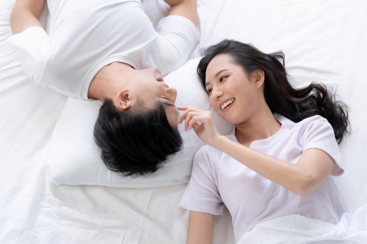 Happy Asian couple lying down smiling and relaxing together in bed.