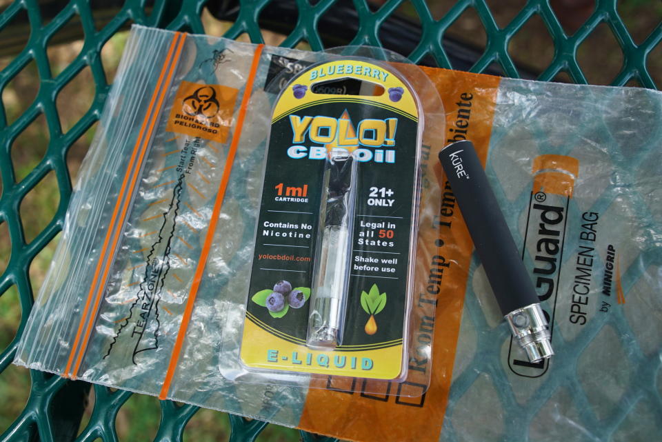 FILE - In this May 8, 2019, file photo, a Yolo! brand CBD oil vape cartridge sits alongside a vape pen on a biohazard bag on a table at a park in Ninety Six, S.C. More than 50 people around Salt Lake City had been poisoned by the time the outbreak ended early last year, most by a vape called Yolo!, the acronym for &quot;you only live once.&quot; (AP Photo/Allen G. Breed, File)