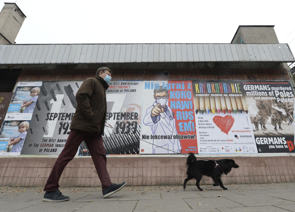 FILE - In this Oct. 16, 2020, file photo, a man passing by a poster warning against neglecting COVID-19 symptoms, in Warsaw, Poland. The European Union still hasn't completely sorted out its messy post-divorce relationship with Britain — but it has already been plunged into another major crisis. This time the 27-member union is being tested as Poland and Hungary block passage of its budget for the next seven years and an ambitious package aimed at rescuing economies ravaged by the coronavirus pandemic. (AP Photo/Czarek Sokolowski, File)