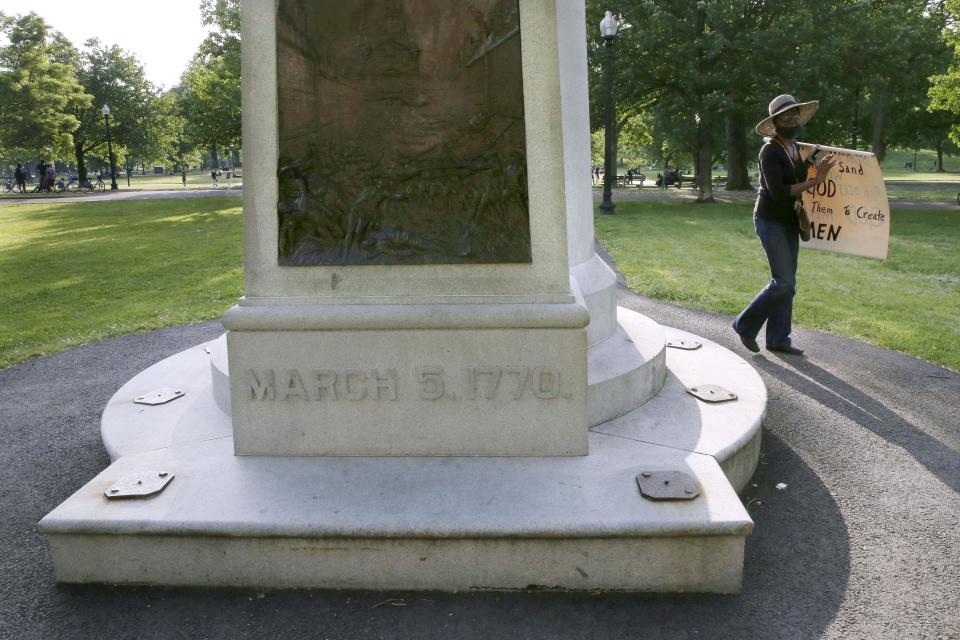 In this Wednesday, June 3, 2020 photo, a woman walks past the Boston Massacre Monument on Boston Common after a protest against police brutality in Boston, following the death of George Floyd, who died after being restrained by Minneapolis police officers on Memorial Day. The relief sculpture on the monument depicts Crispus Attucks, a black man and first person gunned down by British troops during the Boston Massacre on March 5, 1770. The attack helped touch off the American Revolution. (AP Photo/Charles Krupa)