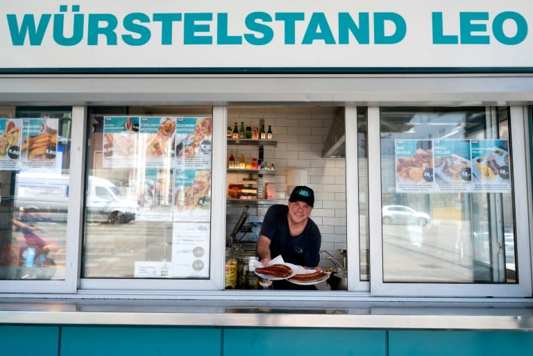 Patrick Bernhardt, employé du plus ancien stand de saucisses de Vienne, "Wuerstelstand LEO", pose pour une photo avec des assiettes de saucisses à Vienne, en Autriche, le 18 juin 2024 (Joe Klamar)