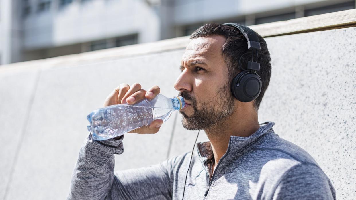 man having a break from exercising wearing headphones and drinking from bottle