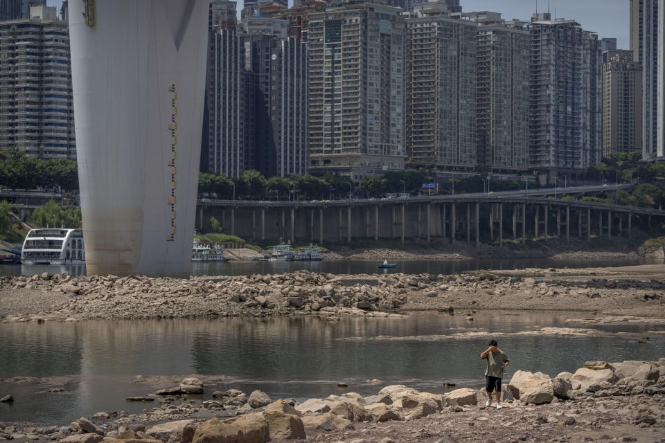 A man wipes his forehead as he walks along the lower than normal bank of the Jialing River in southwestern China's Chongqing Municipality, Friday, Aug. 19, 2022. Ships crept down the middle of the Yangtze on Friday after the driest summer in six decades left one of the mightiest rivers shrunk to barely half its normal width and set off a scramble to contain damage to a weak economy in a politically sensitive year. (AP Photo/Mark Schiefelbein)