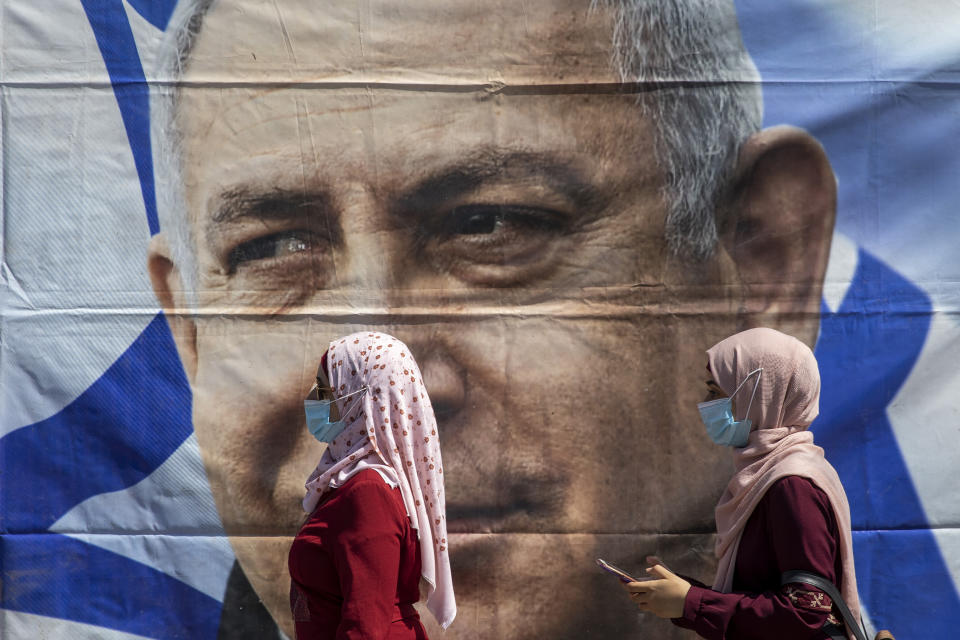 Muslim women wear face masks to help protect themselves from the coronavirus, walk past a poster hung by supporters of Prime Minister Benjamin Netanyahu outside the district court in Jerusalem, Sunday, July 19, 2020. The corruption trial of Netanyahu has resumed following a two-month hiatus. (AP Photo/Ariel Schalit)