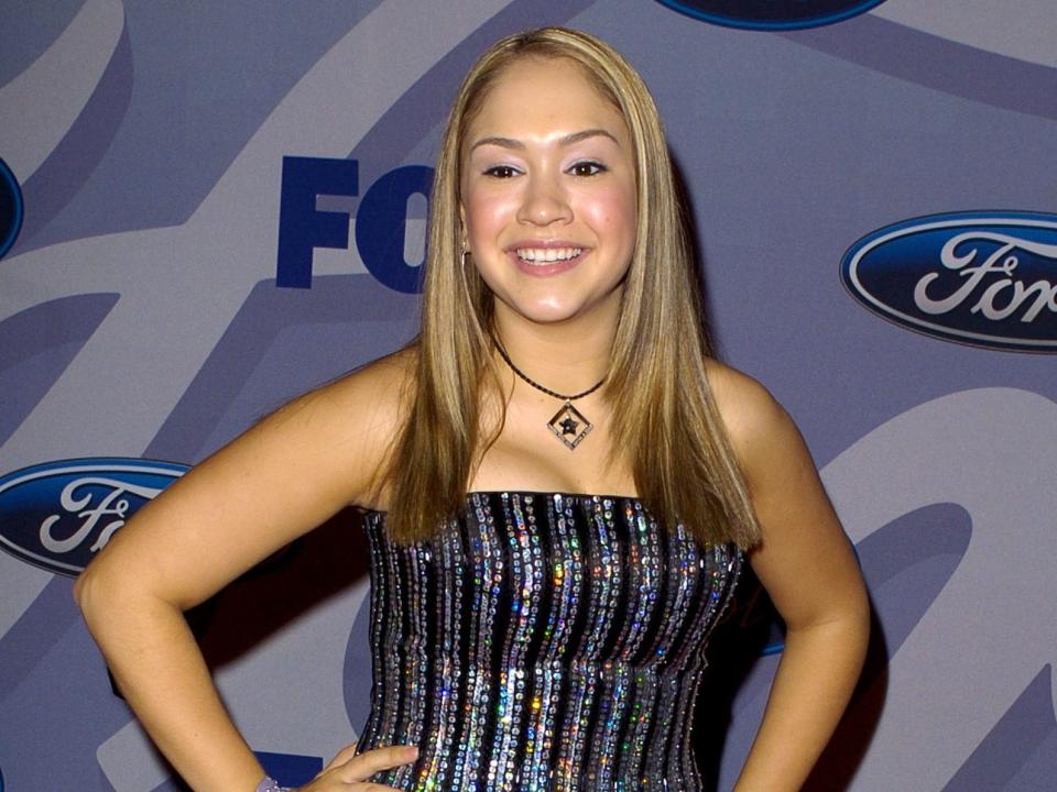 Diana DeGarmo stands with her hands on her hips on the red carpet wearing a sparkly purple and black striped corset