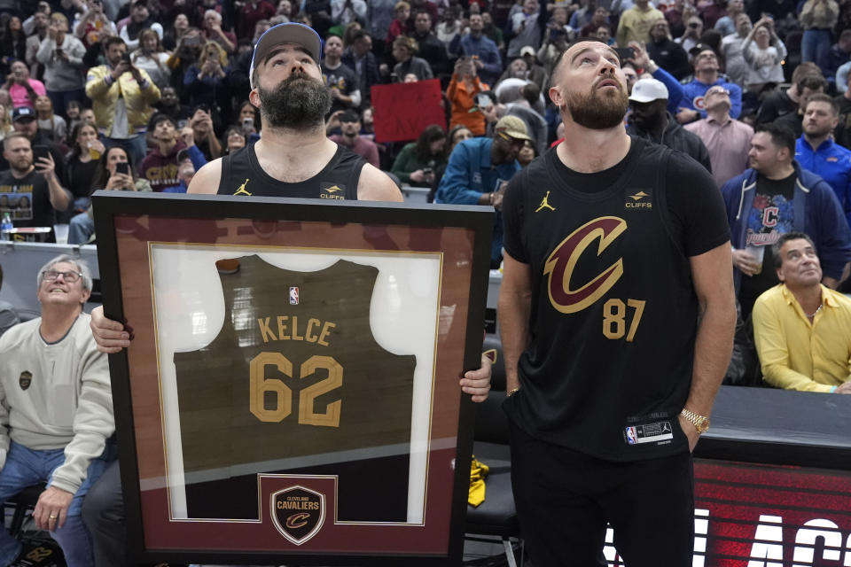 Jason Kelce, left, and Travis Kelce, right, watch a video during a time out at the Celtics-Cavaliers NBA basketball game, Tuesday, March 5, 2024, in Cleveland .Jason Kelce was given a framed jersey. (AP Photo/Sue Ogrocki)
