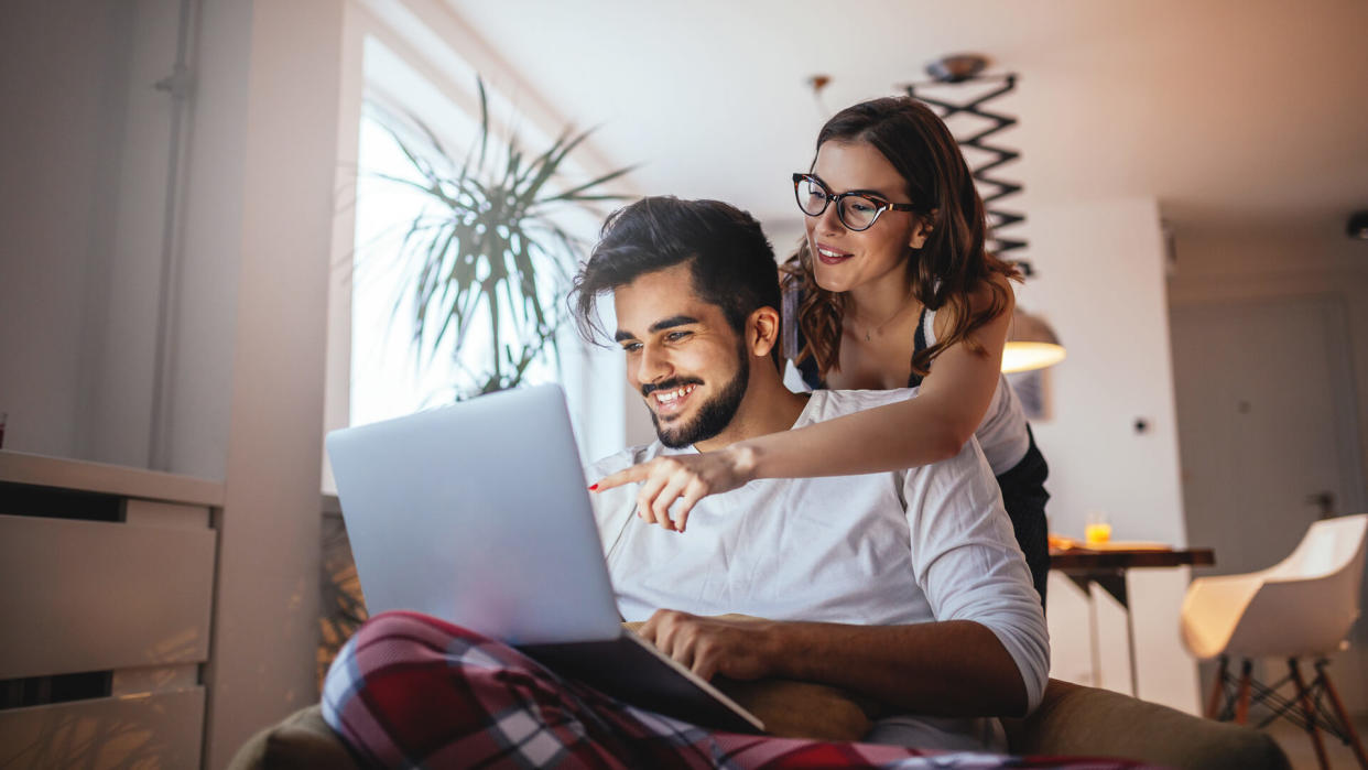 Shot of a happy young couple embracing while using laptop at home.