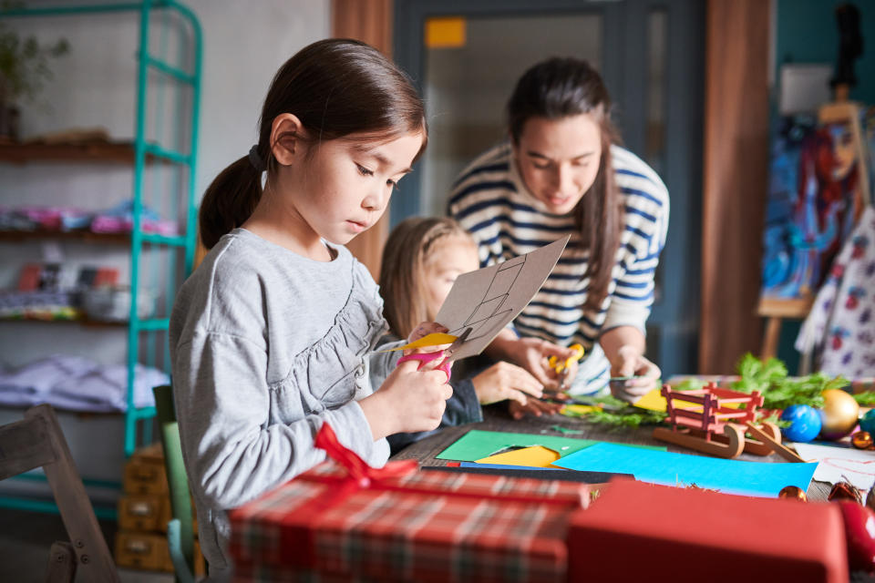 Side view portrait of cute Asian girl making handmade Christmas gifts in art and craft class, copy space