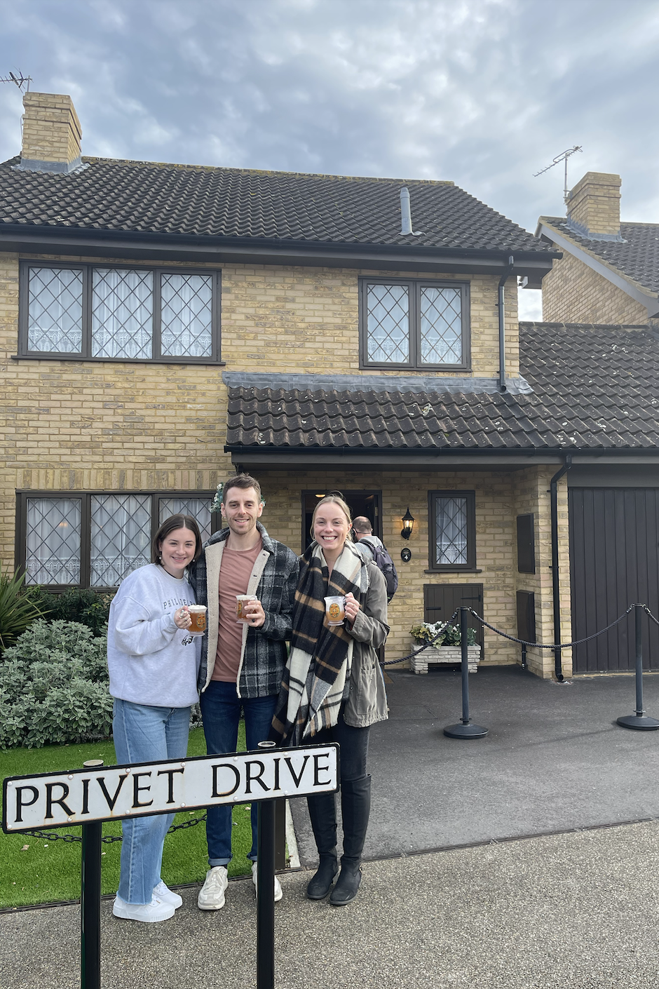 Two friends and myself smiling in front of the Dursley's house with butterbeer drinks in our hands