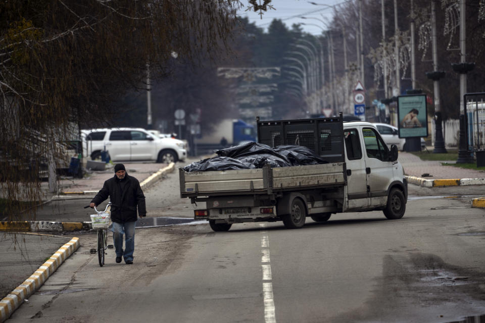 A man walks with a bicycle next to a truck that carries black bags with corpses of people killed during the war with Russia and exhumed from a mass grave for investigations in Bucha, in the outskirts of Kyiv, Ukraine, Monday, April 11, 2022. (AP Photo/Rodrigo Abd)
