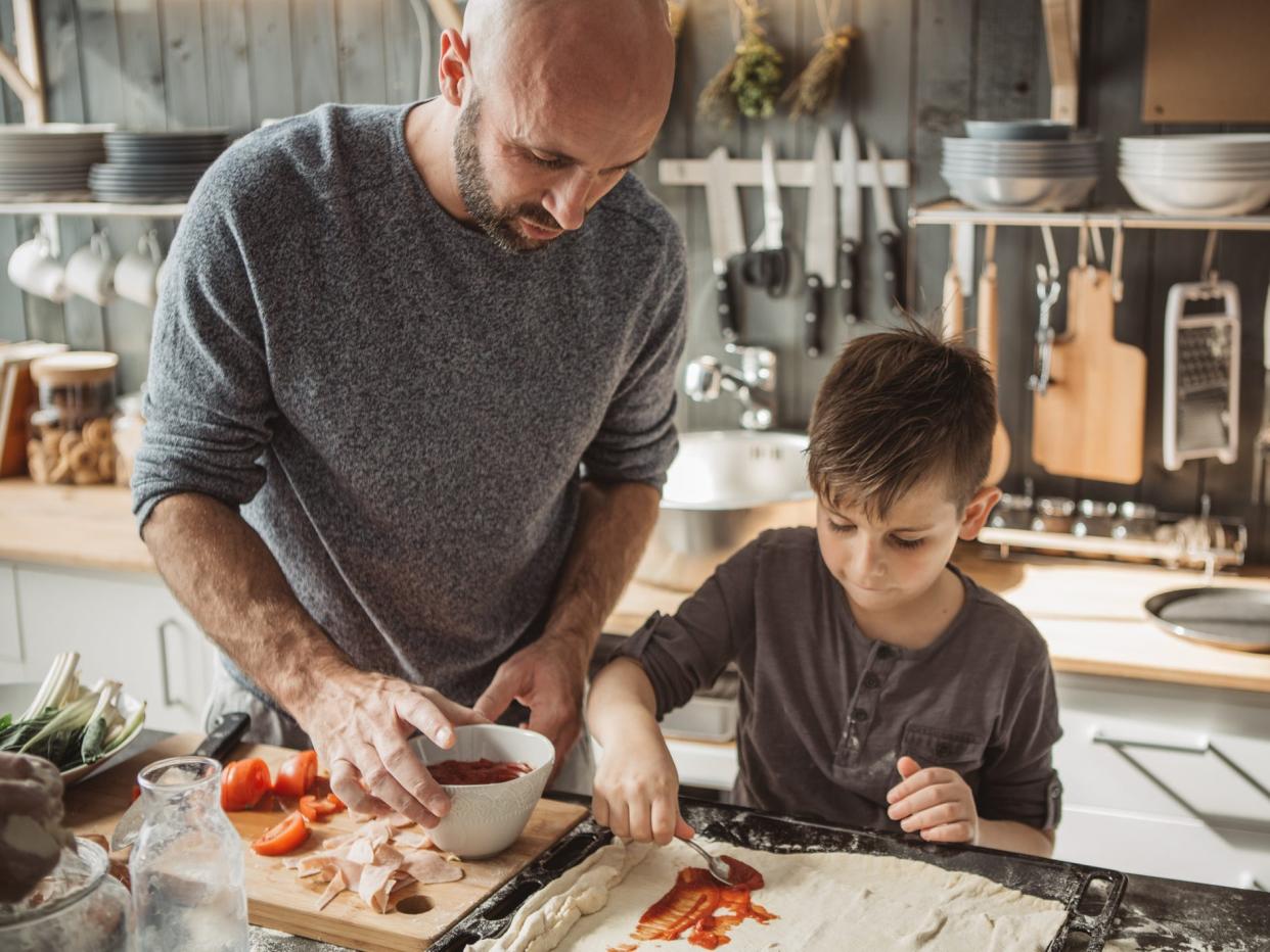 a father and son cooking pizza together in the kitchen