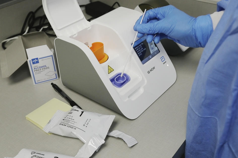 FILE - In this April 10, 2020, file image made from video, a lab technician dips a sample into the Abbott Laboratories ID Now testing machine at the Detroit Health Center in Detroit. Federal health officials are warning about potential accuracy problems with the rapid test for COVID-19 used at thousands of hospitals, clinics and testing sites across the U.S., including the White House. (AP Photo/Carlos Osorio, File)