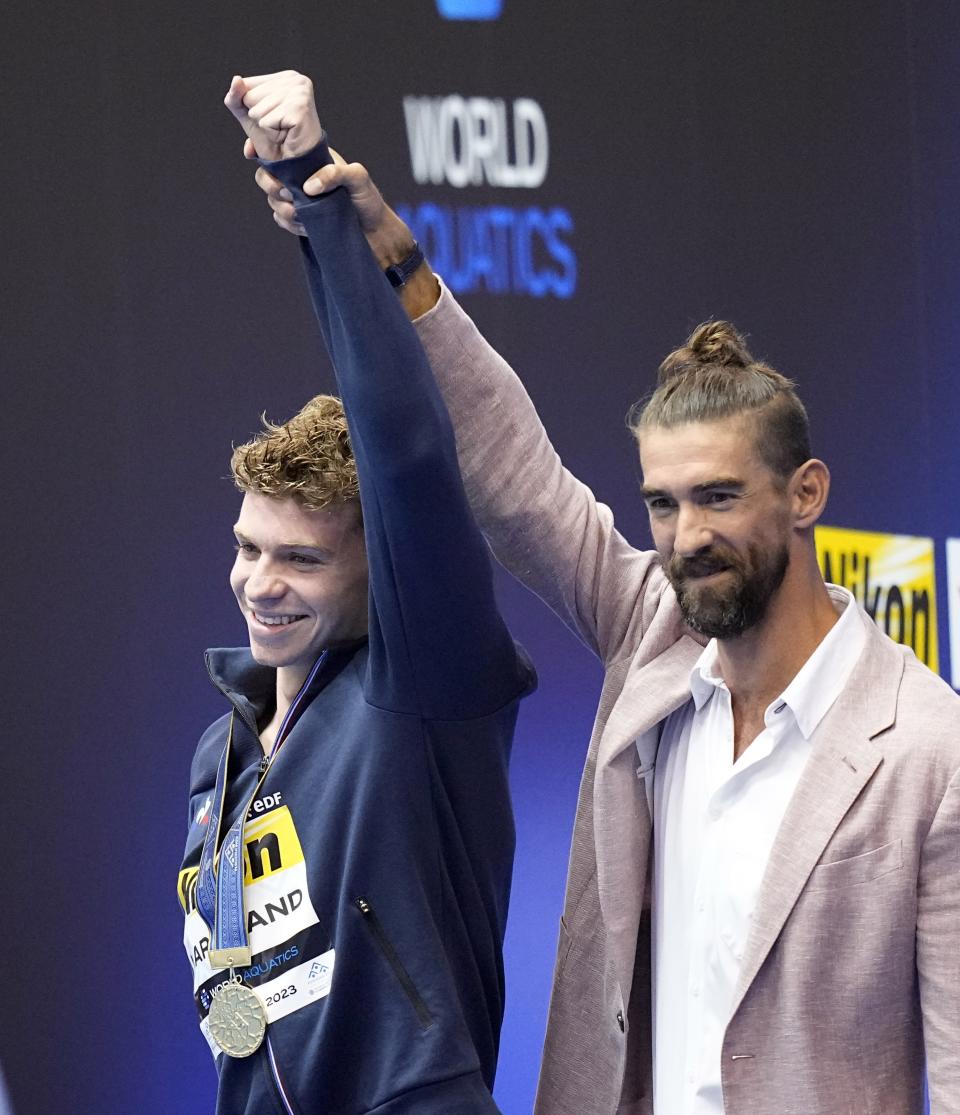 Swimming great Michael Phelps, right, hold up the arm of Leon Marchand, of France, during a medal ceremony for the men's 400m individual medley final at the World Swimming Championships in Fukuoka, Japan, Sunday, July 23, 2023. Marchand won gold setting a new world record, breaking Phelps' 2008 record. (AP Photo/David J. Phillip)