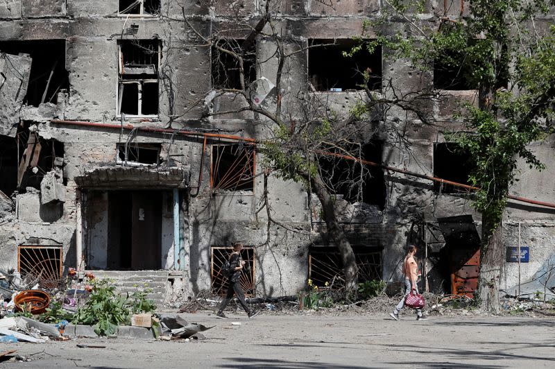 FILE PHOTO: FILE PHOTO: People walk past a heavily damaged residential building in Mariupol