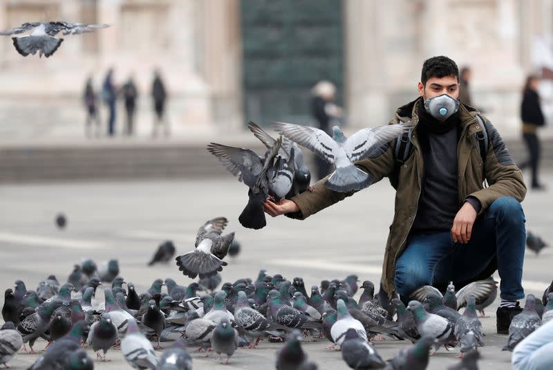 Man in a face mask feeds pigeons in Milan