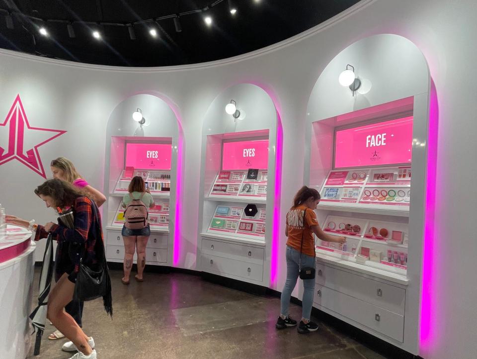 pink-lit white curved walls inside Jeffree Star store with a few individuals looking at products within the shelves