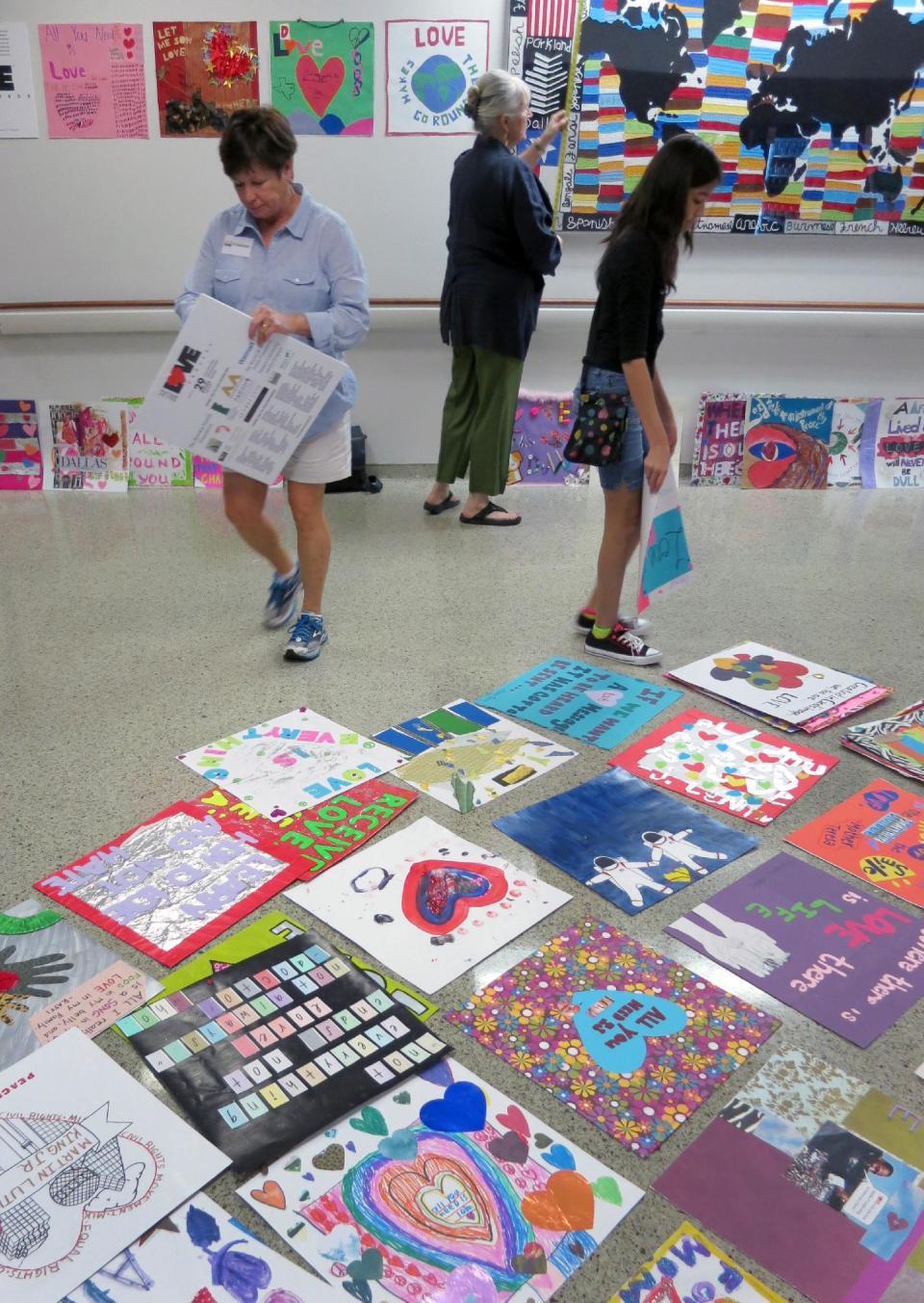 Becky Crawford, left, director of experiential education and service learning at Parish Episcopal School, Karen Blessen, center, founder of the nonprofit 29 Pieces and executive director of the Dallas LOVE Project and 13-year-old Melissa Serrano, right, hang art in the hallways at Parkland Memorial Hospital, Saturday Sept. 21, 2013 in Dallas. About 30,000 works of art reflecting on love will be displayed throughout Dallas this fall to commemorate the 50th anniversary of the assassination of President John F. Kennedy. (AP Photo/29 Pieces)