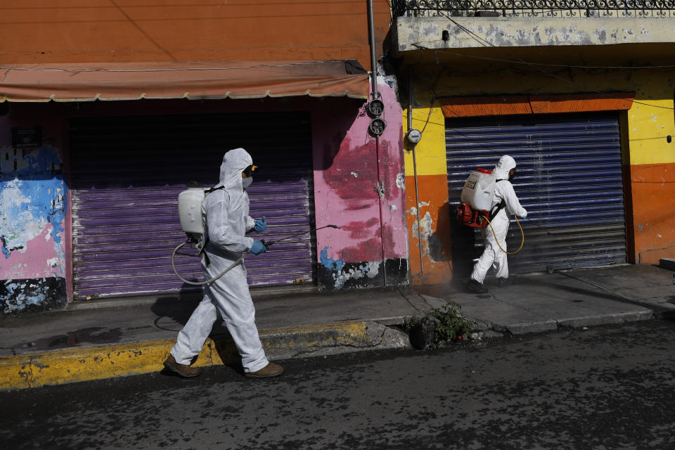 FILE - In this July 24, 2020 file photo, workers spray a disinfectant solution on a street in San Gregorio Atlapulco in the Xochimilco district of Mexico City, amid the new coronavirus pandemic. In San Gregorio and many places like it, fear of hospitals, deep-rooted distrust of authorities, difficulties accessing medical care, and the pressure to make a living amid economic uncertainty are fueling the spread of the virus. (AP Photo/Rebecca Blackwell, File)