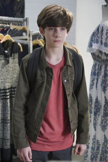 A teen boy stands amid racks of women's clothing on a TV show