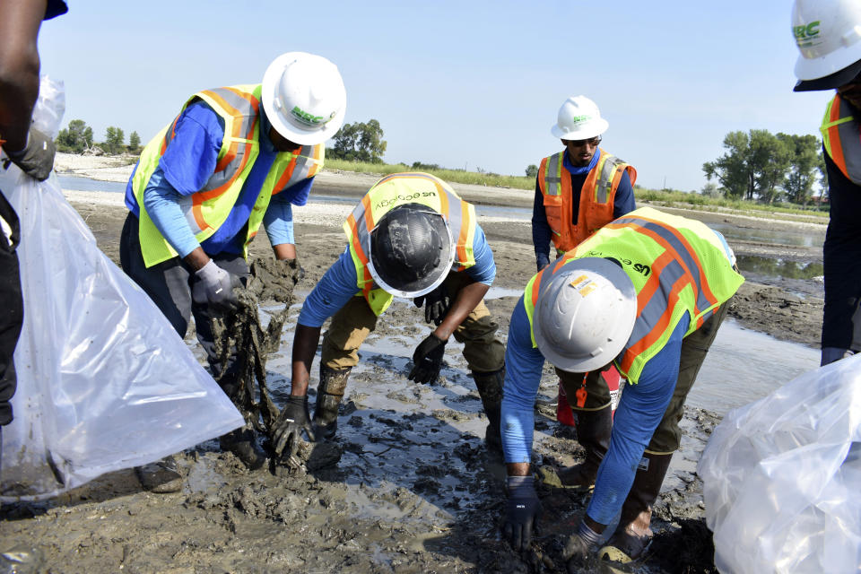 Cleanup workers load bags of oil products collected along the Yellowstone River onto a boat, Thursday, July 20, 2023, near Laurel, Montana. Tar balls have been found 100 miles downstream of the site of a June 24 bridge collapse and train derailment that sent hazardous material tank cars plummeting into the river. (AP Photo/Matthew Brown)