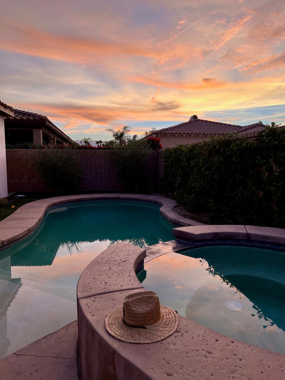 A pool at sunset with a hat on the ledge.