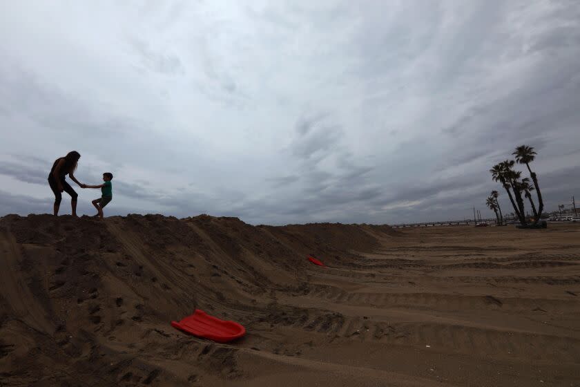 SEAL BEACH, CA - SEPTEMBER 10, 2022 - - Nadia Davis plays with her sun Elijah, 6, on a berm that prevented tidal flooding to nearby homes as remnants of Tropical Storm Kay hang overhead in Seal Beach on September 10, 2022. Lingering rains from Kay's remnants are raising concerns about possible flooding in Southern California on Sunday and early into the week, according to the National Weather Service. (Genaro Molina / Los Angeles Times)