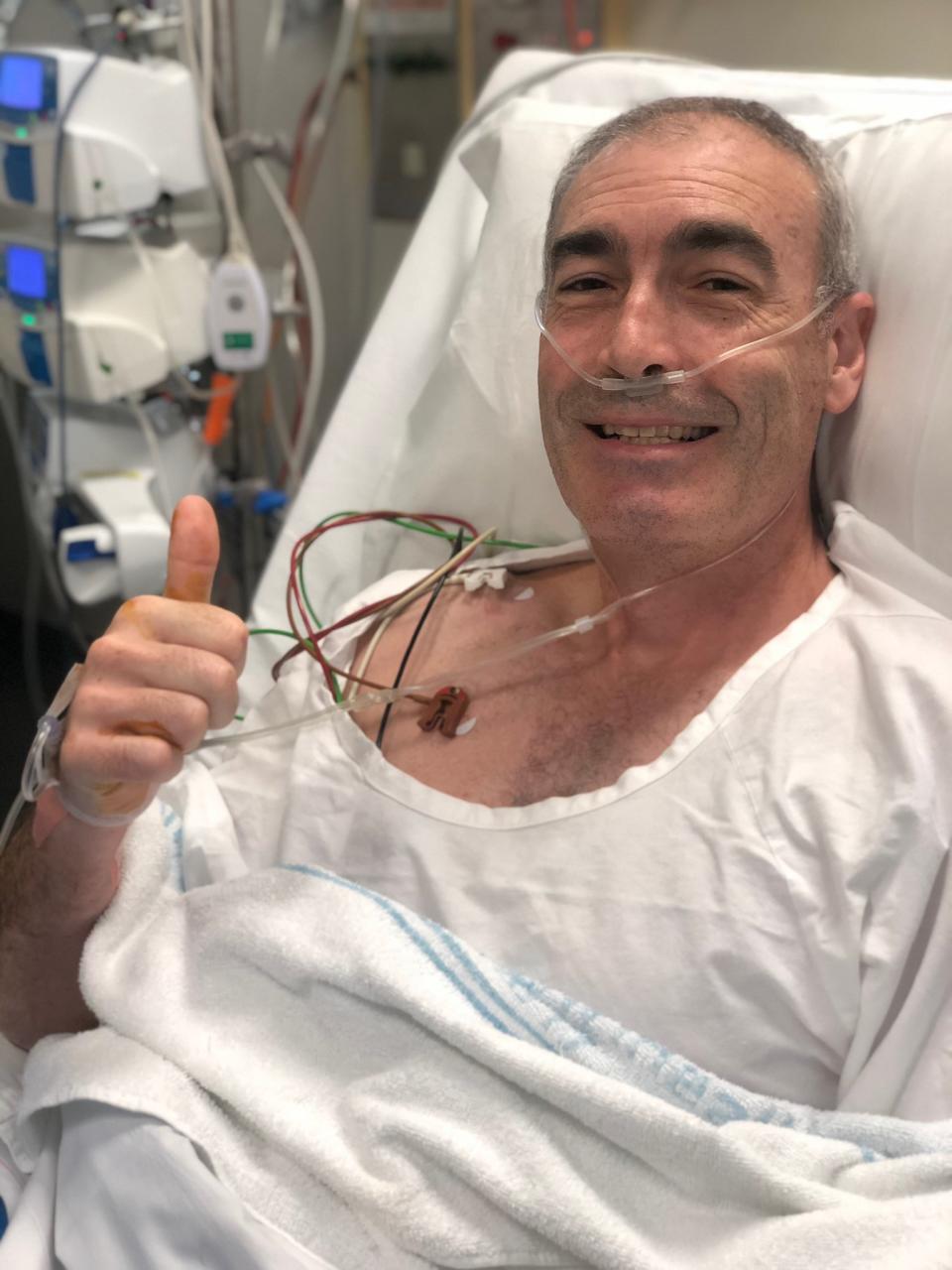 Yellow Wiggle Greg Page wears a white hospital gown in bed while recovering in hospital after suffering a cardiac arrest on stage on January 17, 2020