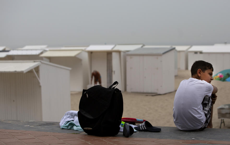 A boy waits with his backpack on the promenade overlooking the beach at the Belgian seaside resort of Blankenberge, Belgium, Tuesday, Aug. 11, 2020. A skirmish took place on the beach on Saturday, Aug. 8, 2020 which resulted in two coastal communities banning day trippers from the city. (AP Photo/Virginia Mayo)