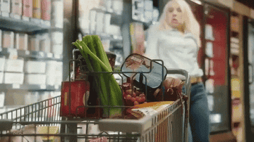 Kate McKinnon tosses a grocery item into a cart in a "Saturday Night Live" sketch