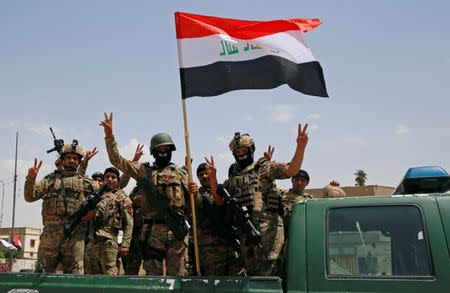 Members of Iraqi forces make a "V" sign and display an Iraqi flag as they arrive to take part in a victory celebration after defeating the Islamic State militants and retaking the Grand al-Nuri Mosque in the Old City in Mosul, Iraq July 2, 2017. REUTERS/Erik De Castro