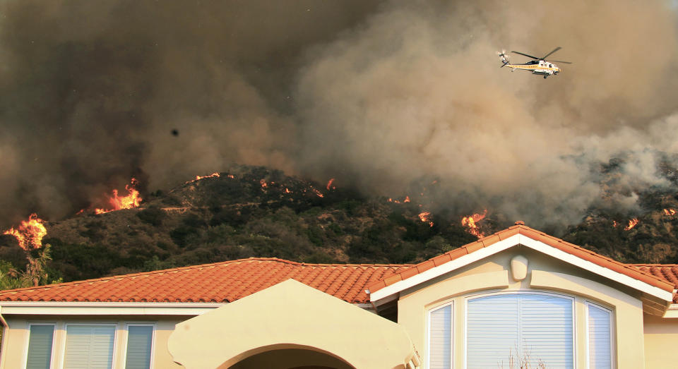 A firefighting helicopter passes over the hills behind homes as a wildfire burns just north of the San Gabriel Valley community of Glendora, Calif., on Thursday, Jan 16, 2014. Southern California authorities have ordered the evacuation of homes at the edge of a fast-moving wildfire burning in the dangerously dry foothills of the San Gabriel Mountains. (AP Photo/Ringo H.W. Chiu)